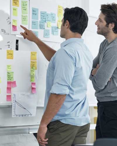 Two people looking at a post-it white board represents the agility of processes and successful solutions