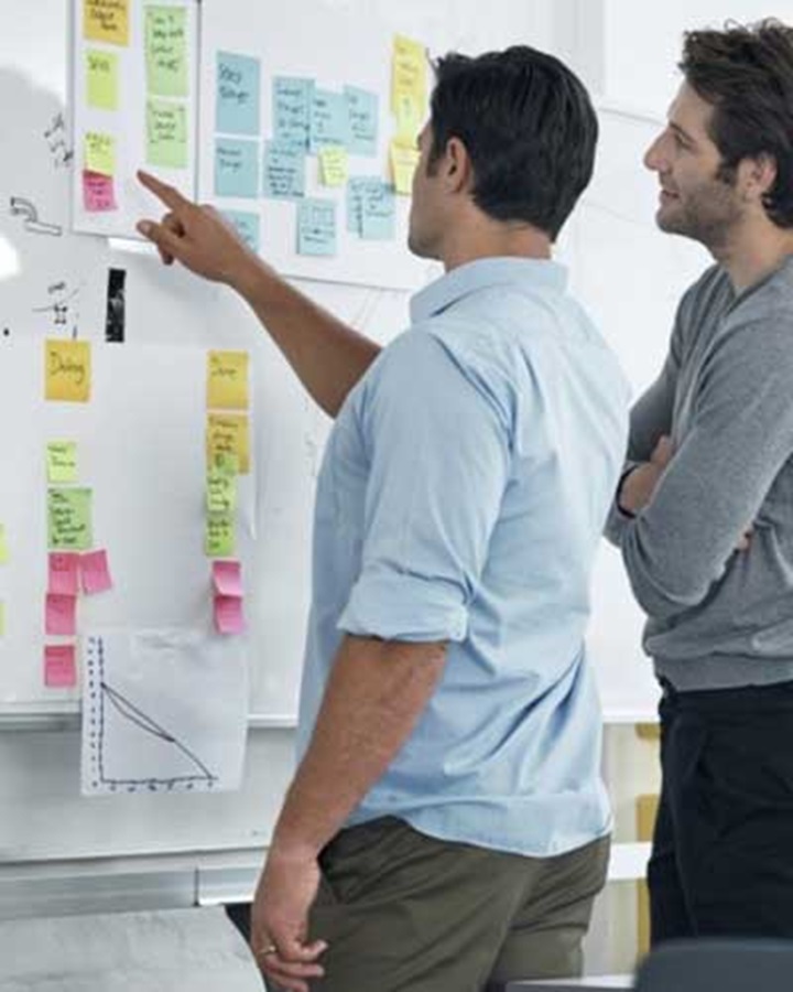 Duas pessoas a olhar para um quadro com post-its representando a agilidade dos processos e soluções de sucesso