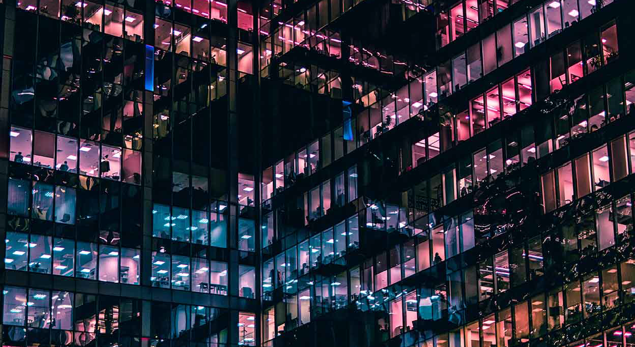 Janelas de um edificio de escritórios iluminadas durante a noite representando a nossa solução de análise de oportunidades e performance de vendas